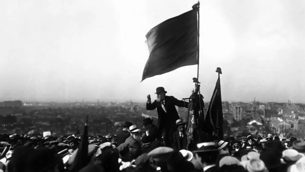 Discours de Jaurès sous un drapeau rouge au Pré-Saint-Gervais, lors de la manifestation contre la loi des Trois ans, 25 mai 1913. © Maurice-Louis Branger / Domaine public.